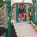 Young boy poised to go down roller slide at inclusive playground